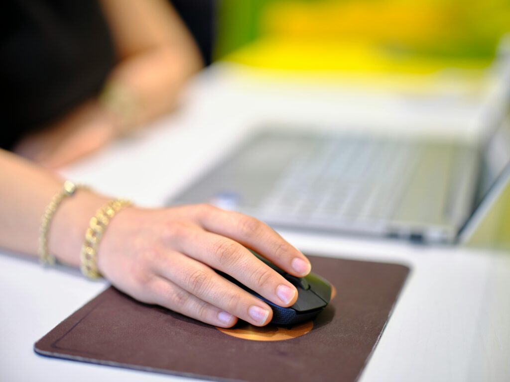 "Mano utilizando un mouse sobre una alfombrilla ergonómica frente a un portátil"